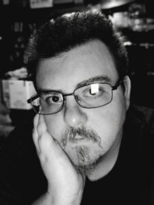 A man with a goatee and glasses with his hand resting against the side of his face.