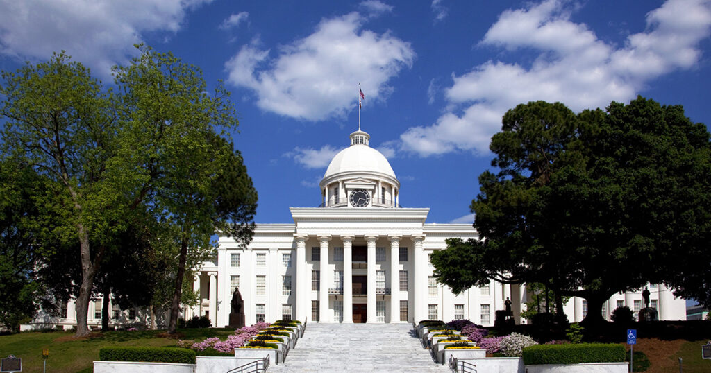 The Alabama State Capitol building in Montgomery with white columns and a gold dome beneath a bright blue sky.