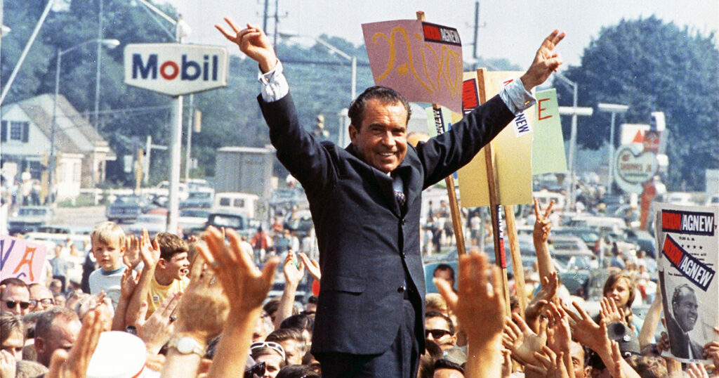 Richard Nixon speaking at an outdoor campaign rally during the 1968 presidential election with campaign signs visible behind him.