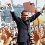 Richard Nixon speaking at an outdoor campaign rally during the 1968 presidential election with campaign signs visible behind him.