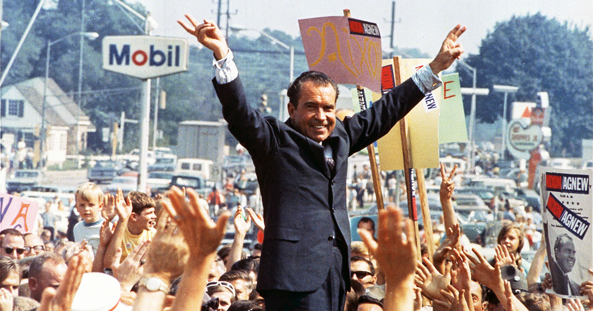 Richard Nixon speaking at an outdoor campaign rally during the 1968 presidential election with campaign signs visible behind him.